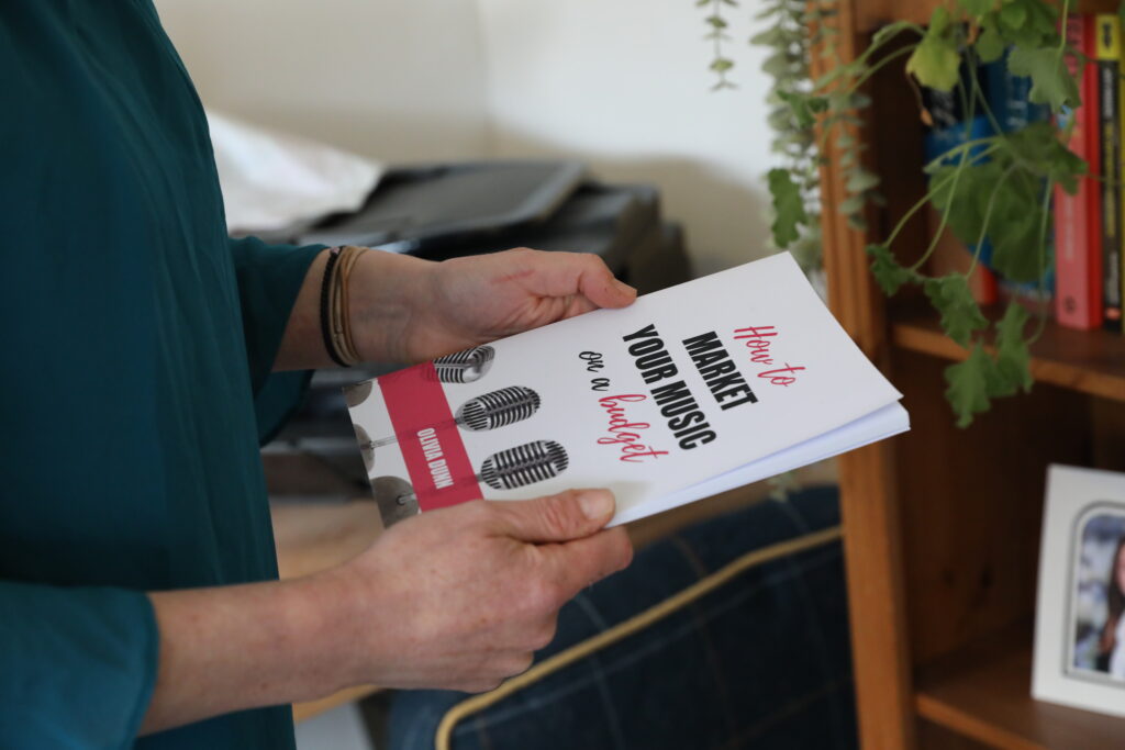 Hands holding a book called 'How to Market Your Music on a Budget'