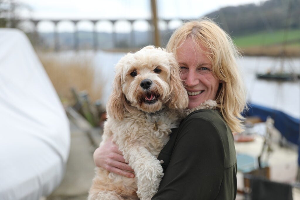 Olivia Dunn holding her dog Cassie in front of the river Tamar with Calstock Viaduct in the background